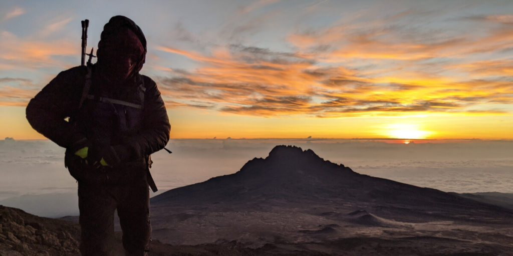 Man in black jacket with incredible Kilimanjaro summit sunset behind 